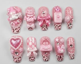 Peut inclure: Un ensemble de dix faux ongles roses avec divers motifs. Certains ongles présentent des nœuds, des cœurs et un téléphone, tandis que d'autres ont un motif à carreaux ou un lapin. Les pointes des ongles ont un imprimé léopard.