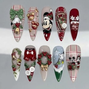 May include: A set of ten press-on nails featuring Christmas-themed Mickey Mouse designs. The nails display various holiday motifs including a green bow, gold bells, a wreath, a sled, a chimney, and Mickey Mouse characters in red, white, and green colors.