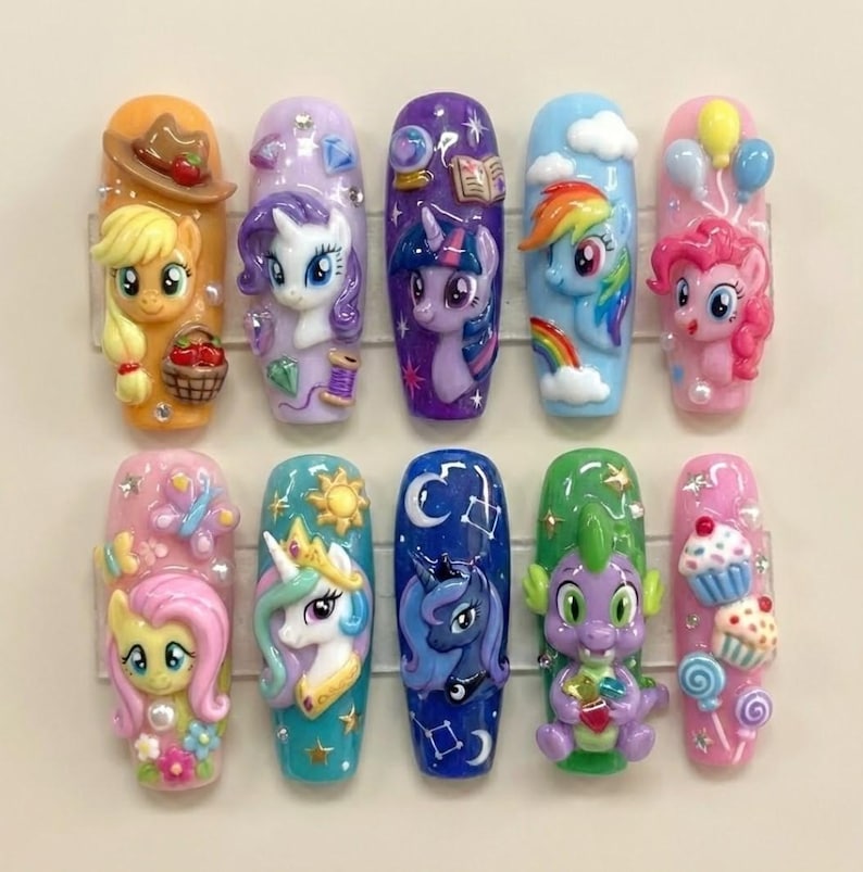 May include: A set of ten sculpted nail art designs featuring colorful My Little Pony characters. Each nail showcases a different character with intricate details, including a cowboy hat, rainbow, and cupcakes. The nails are set against a neutral background.
