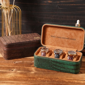 May include: A green rectangular watch case with a crocodile-embossed texture, featuring a tan interior holding three wristwatches and the text "Make every second count." A closed brown crocodile-embossed watch case sits beside it.