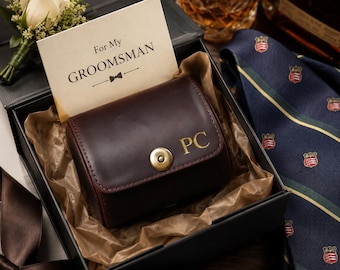 Pode incluir: Um estojo de couro castanho escuro para relógio com as iniciais douradas PC e um fecho de latão, dentro de uma caixa de presente preta com um cartão escrito For My GROOMSMAN, uma flor de lapela de rosa branca e uma gravata azul-marinho.