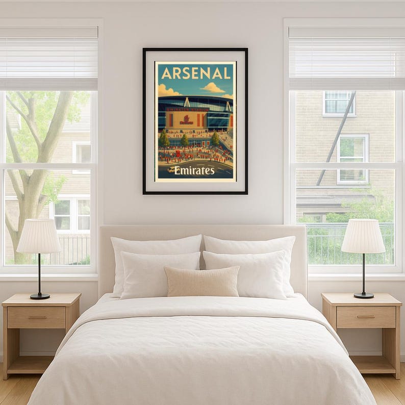 May include: A framed poster featuring the Emirates Stadium, home of Arsenal Football Club. The poster has a vintage travel-poster style with the word "ARSENAL" at the top and "Emirates" at the bottom. The image is set in a bedroom with a bed, nightstands, and lamps.