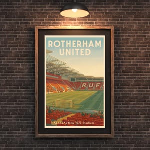 Puede incluir: Póster enmarcado con una ilustración de un estadio, que muestra "ROTHERHAM UNITED" en azul claro. La obra de arte muestra un campo de fútbol con asientos rojos y el texto "AESSEAL New York Stadium" en la parte inferior. El marco es marrón.