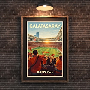 Może przedstawiać: Oprawiony plakat przedstawiający scenę ze stadionu z napisem "GALATASARAY" i "RAMS Park". Grafika przedstawia boisko do piłki nożnej z kibicami w pomarańczowych koszulkach machających czerwonymi flagami. Plakat jest w ciemnej drewnianej ramie, zawieszony na ceglanej ścianie.
