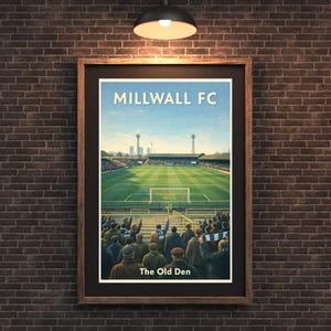 Pode incluir: Impressão emoldurada de um estádio de futebol com o texto "MILLWALL FC" e "The Old Den". A obra de arte retrata um campo verde, arquibancadas cheias de fãs e um céu azul. A moldura é marrom.