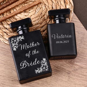 May include: Two black rectangular perfume bottles with black caps. One bottle has the words "Mother of the Bride" and floral accents. The other bottle is inscribed with the name "Victoria" and the date "09.06.2025".