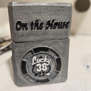 May include: A grey, rectangular box with the words "On the House" embossed on the top. The bottom section features a casino chip design with "Lucky 38" and a spade symbol.