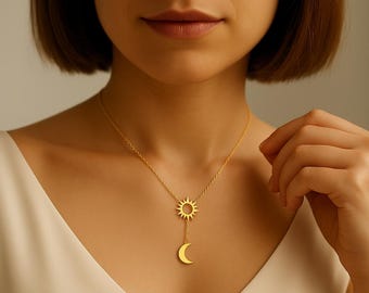 May include: A gold-colored necklace featuring a sun and moon pendant. The sun pendant is a detailed, openwork design, while the moon is a simple crescent shape. The necklace is worn on a person's neck, against a white top.