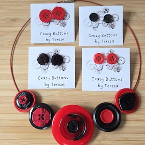 Op de afbeelding: Een ketting- en oorbellen set met grote, kleurrijke knopen. De ketting heeft een rood koord en een verscheidenheid aan rode en zwarte knopen. De oorbellen worden gepresenteerd op kaarten met "Crazy Buttons by Tereza".