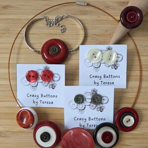 Könnte beinhalten: Eine Auswahl an handgefertigtem Schmuck und Accessoires mit Knöpfen. Das Bild zeigt ein Armband, eine Halskette und Ohrringe sowie einzelne Knöpfe in verschiedenen Farben, darunter Rot, Weiß und Grün. Der Text "Crazy Buttons by Tereza" ist auf den Karten zu sehen.