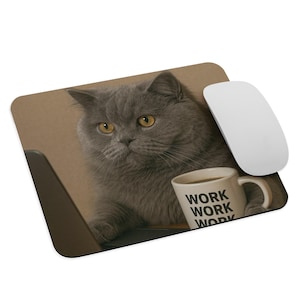 Pode incluir: Um mousepad com um gato cinza com olhos amarelos, olhando para um laptop. Um mouse branco está à direita. Uma caneca de café com a palavra "WORK" repetida três vezes está ao lado do gato. O fundo é marrom claro.