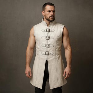 May include: Cream-colored leather vest with a high collar and sleeveless design. The vest features four decorative buckles down the front and a belt around the waist. The stitching is visible, and the vest has a tailored fit.