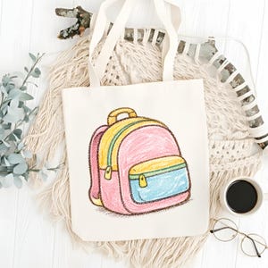 May include: A cream-colored tote bag featuring a colorful illustration of a backpack. The backpack design includes pink, yellow, and blue accents, with a yellow zipper and handle. The bag has cream-colored handles and is set against a neutral background.