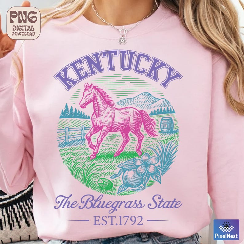 May include: Pink sweatshirt with a graphic of a pink horse, mountains, and the text "Kentucky". The design includes the words "The Bluegrass State" and "EST.1792". The sweatshirt is a light pink color.
