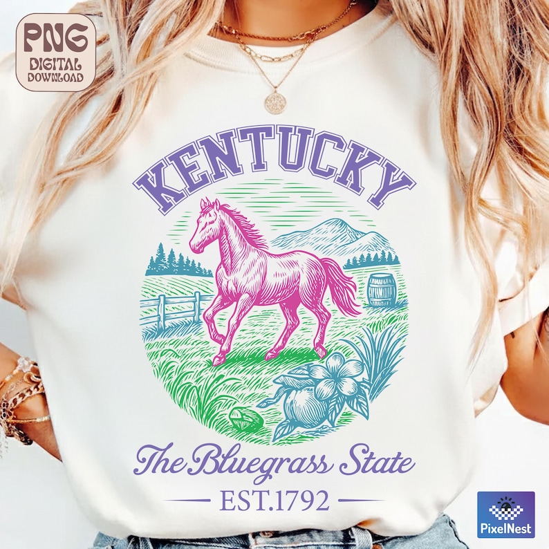 May include: Cream-colored t-shirt featuring a graphic of a pink horse within a circle, with the word "Kentucky" above. Below, it reads "The Bluegrass State" and "EST.1792". The design includes a barrel, flowers, and a fence.