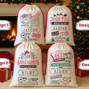 May include: Four white Christmas Santa sacks with red trim, each featuring unique designs. The sacks have festive graphics and text, including "Santa Express" and personalized names. A Christmas tree and fireplace are in the background.