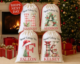 May include: Four personalized Christmas gift bags with red trim and drawstring closures. Each bag features a large letter, name, and festive holiday illustrations. The bags are displayed in front of a fireplace and Christmas tree.