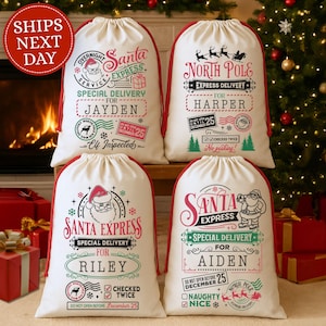May include: Four white Christmas Santa sacks with red trim and drawstring closures. Each sack features festive graphics and text, including "Santa Express" and "North Pole Express" with names like "Jayden" and "Harper". A Christmas tree and fireplace are in the background.