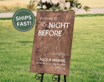 May include: A wooden wedding welcome sign with the text "WELCOME TO The NIGHT BEFORE" in white lettering. The sign also includes the names "ALICE & MICHAEL" and the date "09.29.28". The sign is decorated with flowers.