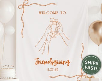May include: White Friendsgiving banner with brown line art of hands toasting champagne glasses. The words "WELCOME TO" and "Friendsgiving" are written in brown script. The date "11.27.25" is also included.