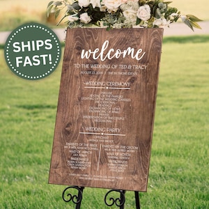 May include: A wooden wedding welcome sign with the names of the couple and ceremony details. The sign is brown with white lettering and is displayed on a black metal stand. A green circle with the words "SHIPS FAST!" is in the upper left corner.