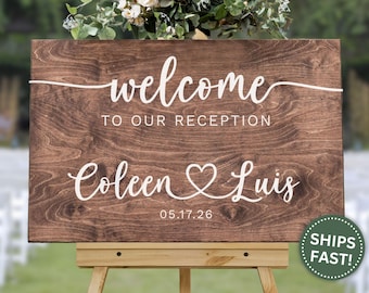 May include: A wooden welcome sign with the words "welcome to our reception" in white script. Below, the names "Coleen & Luis" are displayed with a heart symbol, and the date "05.17.26". The sign is on a wooden easel.
