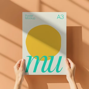 May include: A3 poster mockup held by hands, featuring a large yellow circle and the word "mu" in teal script. The poster is against a peach-colored wall with shadows.