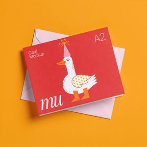 Può includere: Mockup di biglietto A2 rosso con un'oca dei cartoni animati con un cappello da festa, su una busta rosa, su sfondo arancione. La carta ha il testo "Card Mockup" e "mu".