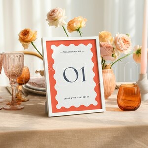 Pu&ograve; includere: Un'apparecchiatura con un segnaposto con cornice bianca con il numero "01". Il segnaposto ha un bordo corallo ed &egrave; circondato da vetreria, fiori e candele. La tavola &egrave; apparecchiata per un evento speciale.