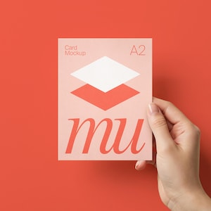 May include: A hand holds a card mockup against a red background. The card features the text "Card Mockup" and "A2" in the upper corners. The design includes a white and coral geometric shape and the word "mu" in a stylized font.