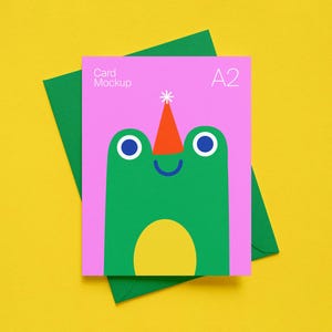 Puede incluir: Maqueta de tarjeta A2 con un diseño de rana verde sobre fondo rosa, con un sobre verde sobre fondo amarillo. La rana tiene ojos azules, nariz naranja y vientre amarillo. La tarjeta dice "Card Mockup" y "A2".