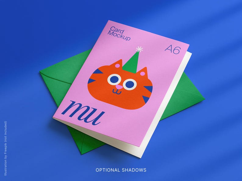 May include: A pink A6 card mockup featuring an orange cartoon cat with a green party hat, on a green envelope. The card has the word "mu" in blue script. The background is a solid blue.