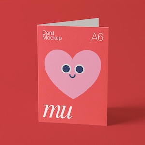 May include: A red A6 card mockup with a pink heart illustration featuring blue eyes and a smiling mouth. The card has the text "Card Mockup" and "mu" in white.