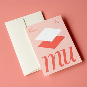 Puede incluir: Maqueta de tarjeta A2 con un diseño coral, con una forma geométrica blanca y coral y la palabra "mu" en coral. Un sobre blanquecino está junto a la tarjeta sobre un fondo coral.