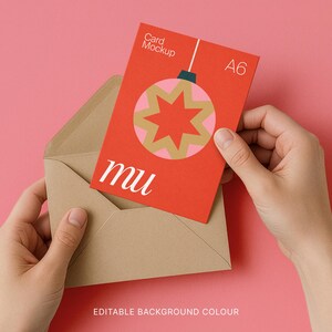 May include: A red A6 card mockup with a Christmas ornament design is held in a brown envelope against a pink background. The card features a gold and pink starburst design and the letters "mu". The words "Card Mockup" and "A6" are also visible.