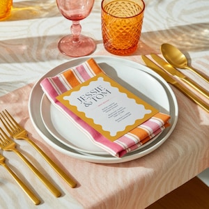 May include: A table setting with white plates, gold cutlery, and striped napkins. A menu with the text "JESSIE & TOM" is on top of the napkin. Pink and orange glasses are also visible.