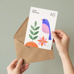 May include: A5 card mockup featuring a colorful bird illustration with a pink body, blue wing, and orange beak. The card is held in a brown envelope. The card also features a green plant and orange flower.