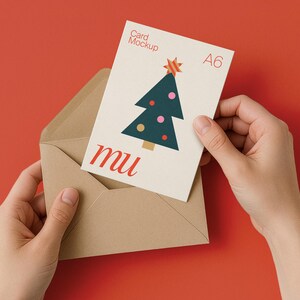 May include: A6 card mockup with a Christmas tree design, held in a kraft paper envelope against a red background. The card features a green tree with pink and yellow ornaments and a star. The word "mu" is printed in red.
