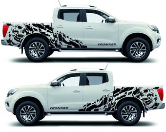 May include: Two white pickup trucks with black skull and abstract design decals. The word "FRONTIER" is printed in black on the side of the truck. The trucks have black wheels and tinted windows.