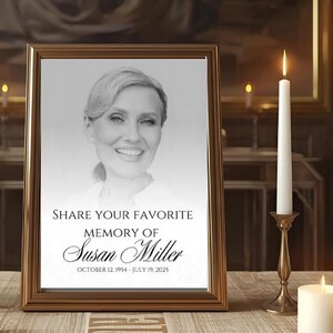 May include: A framed memorial portrait with the text "SHARE YOUR FAVORITE MEMORY OF Susan Miller OCTOBER 12, 1954 - JULY 19, 2025." The portrait is surrounded by lit candles in gold candle holders, set on a table with a patterned tablecloth.