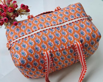 May include: A quilted duffel bag in a vibrant orange fabric featuring a repeating floral pattern in shades of blue and pink. The bag includes a white zip closure along the top and two matching orange and white striped fabric handles.