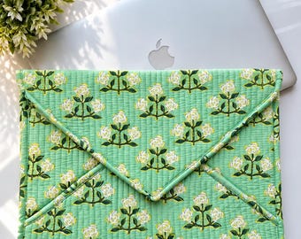 May include: A quilted laptop sleeve in a light green fabric featuring a repeating pattern of white roses with dark green stems and leaves. The sleeve has an envelope-style flap closure with horizontal stitching throughout the entire surface.