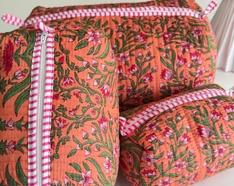 May include: Three quilted pouches in varying sizes featuring an orange fabric base with a repeating floral pattern in shades of pink and green. Each pouch includes a white zipper closure accented with a pink and white striped fabric trim.