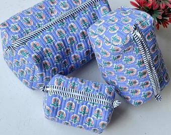 May include: A set of three quilted pouches in varying sizes, featuring a light blue fabric with a repeating floral pattern in pink and green. Each pouch has a white zip with a navy and white striped trim along the closure edge.