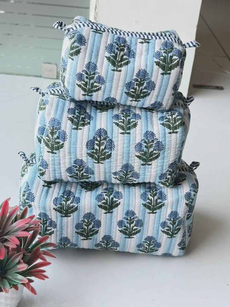 Puede incluir: Un conjunto de tres estuches acolchados rectangulares apilados verticalmente. Cada estuche presenta un patr&oacute;n de rayas verticales en azul claro y blanco con un motivo floral repetitivo en azul y verde oscuro. Textura suave y acolchada.
