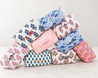 May include: A collection of quilted fabric pouches in various patterns including blue fan shapes, pink floral prints, and pink gingham. Several pouches are personalised with embroidered names or initials like Laura, A/B, Nikkil, Emma, Sarah, and BOHO.