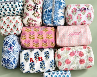 May include: A collection of ten rectangular quilted fabric pouches featuring various floral and geometric patterns in blue, red, pink, and green. Several pouches are personalised with embroidered names or initials including BOHO, LAURA, Nikhil, A B, and M.B.