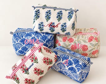 May include: Five quilted fabric pouches with zippered closures, each featuring distinct floral or fan-shaped patterns in blue, red, and pink. Each pouch is personalised with embroidered names or initials including Ash, OMA, MF, Emma, and A.