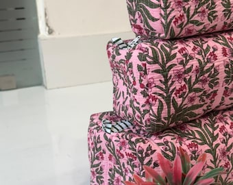 May include: Three rectangular quilted pouches stacked vertically, each featuring a pink fabric base with a repeating dark green and red floral block print pattern. Each pouch includes a small zipper closure with a black and white striped pull tab.