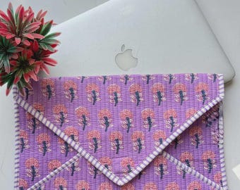 May include: A quilted envelope-style laptop sleeve in a vibrant purple fabric featuring a repeating pattern of small pink and blue floral motifs. The sleeve is finished with a white and purple striped fabric trim along the edges and flap.